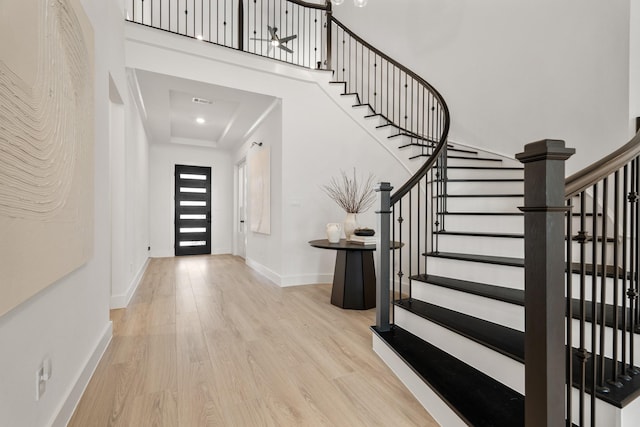 foyer with a raised ceiling, a towering ceiling, and light hardwood / wood-style floors