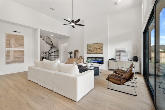 living room featuring a high ceiling, light hardwood / wood-style floors, and ceiling fan