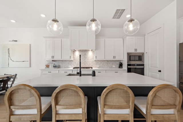 kitchen with white cabinetry, an island with sink, stainless steel appliances, and decorative light fixtures