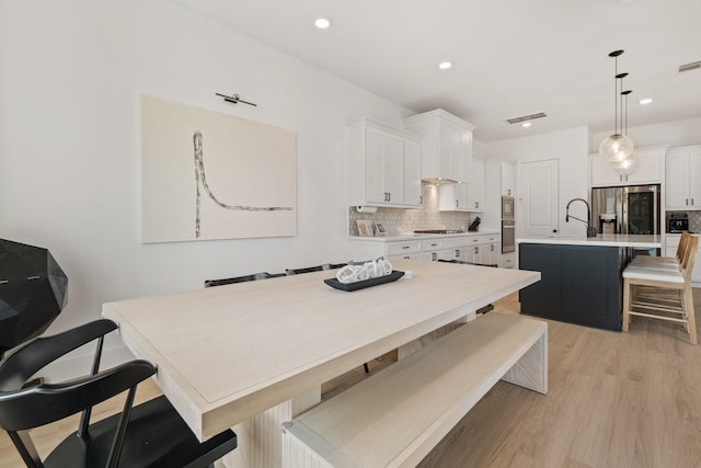 kitchen with pendant lighting, white cabinetry, a kitchen island with sink, and stainless steel refrigerator with ice dispenser