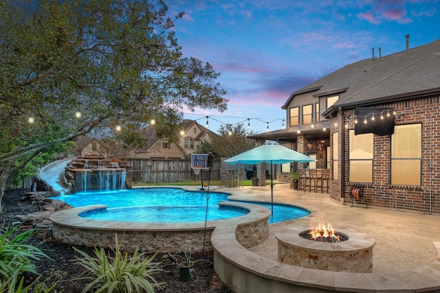 pool at dusk featuring pool water feature, a patio, a fire pit, and an outdoor bar