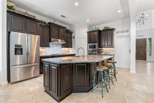 kitchen featuring appliances with stainless steel finishes, dark brown cabinetry, a center island with sink, and sink