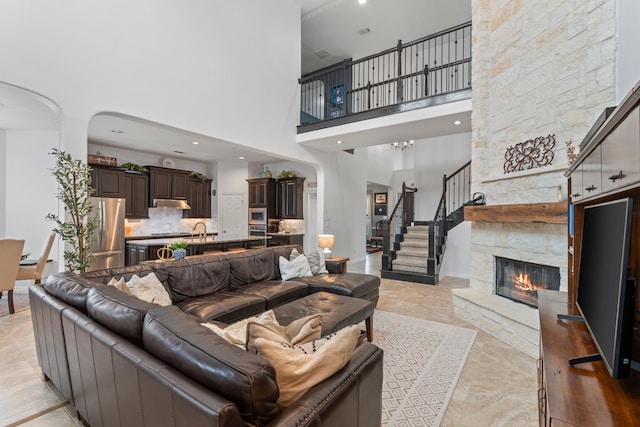 living room featuring a high ceiling, a stone fireplace, a notable chandelier, and sink