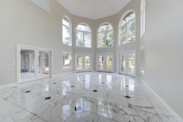 unfurnished living room with french doors, a towering ceiling, and plenty of natural light