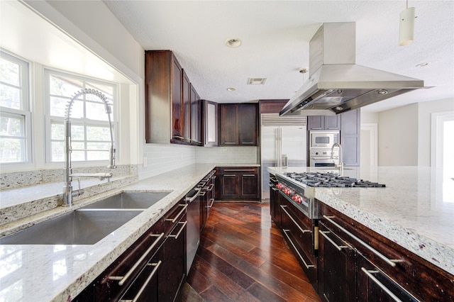 kitchen with sink, light stone counters, ventilation hood, built in appliances, and pendant lighting