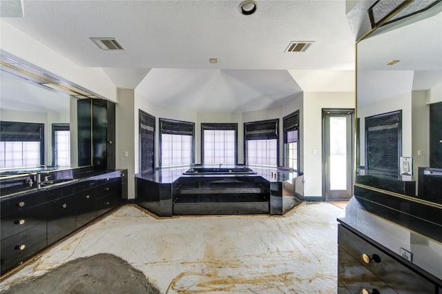 bathroom with vaulted ceiling, a bathtub, vanity, and a textured ceiling