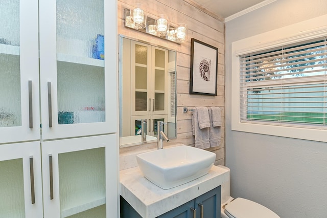 bathroom featuring wooden walls, toilet, vanity, and ornamental molding