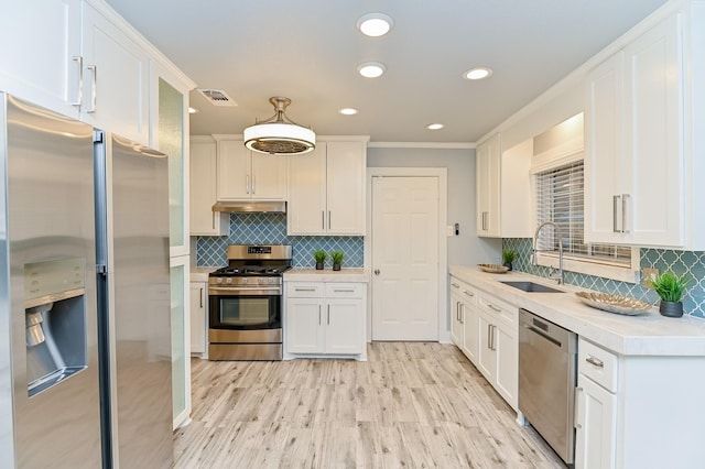 kitchen featuring pendant lighting, white cabinets, sink, light hardwood / wood-style flooring, and stainless steel appliances