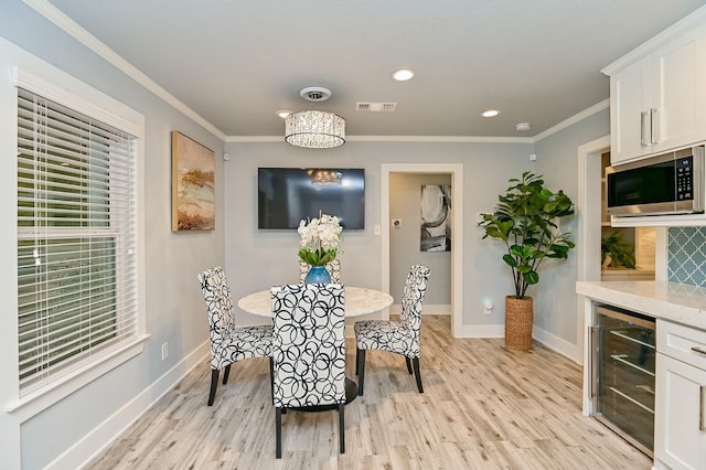 dining space featuring light wood-type flooring, an inviting chandelier, beverage cooler, and ornamental molding