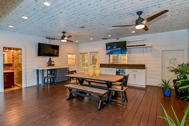 dining space featuring dark hardwood / wood-style flooring, ceiling fan, and wooden walls