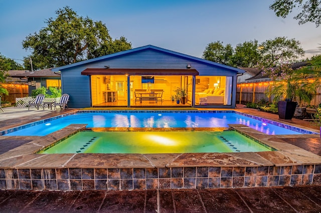 pool at dusk featuring a patio area and an in ground hot tub