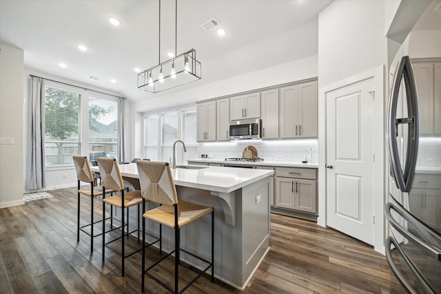 kitchen with gray cabinets, a center island with sink, and appliances with stainless steel finishes