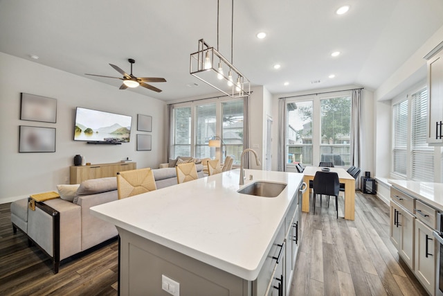 kitchen with ceiling fan, sink, wood-type flooring, decorative light fixtures, and an island with sink