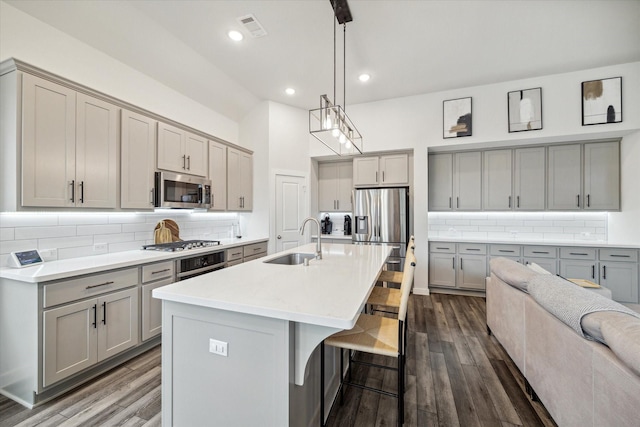 kitchen with sink, backsplash, decorative light fixtures, a center island with sink, and appliances with stainless steel finishes