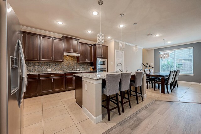 kitchen featuring light stone countertops, appliances with stainless steel finishes, a kitchen island with sink, hanging light fixtures, and a breakfast bar area