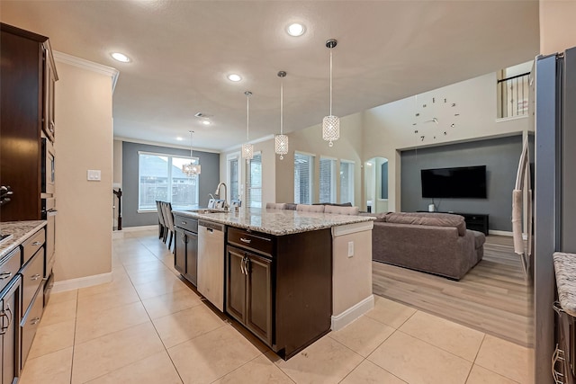 kitchen with dark brown cabinetry, stainless steel appliances, light stone counters, an island with sink, and pendant lighting