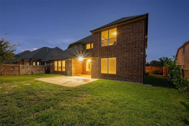 back house at dusk featuring a lawn and a patio