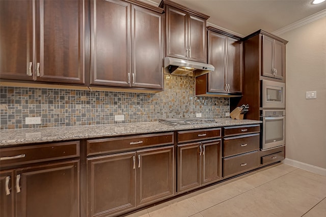 kitchen with appliances with stainless steel finishes, backsplash, light stone counters, crown molding, and light tile patterned flooring