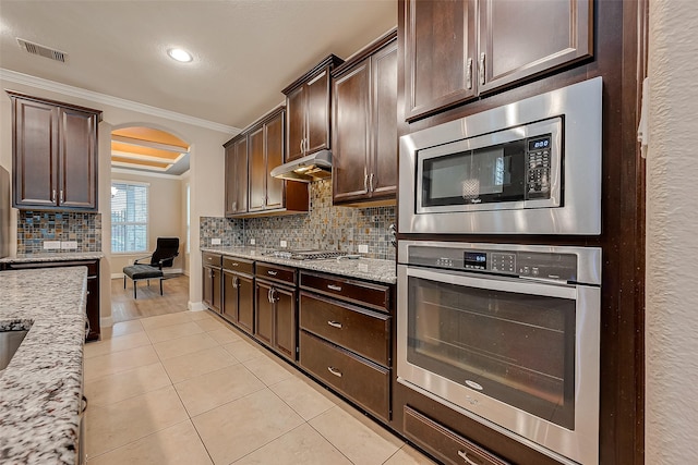 kitchen with light stone countertops, dark brown cabinets, stainless steel appliances, and ornamental molding