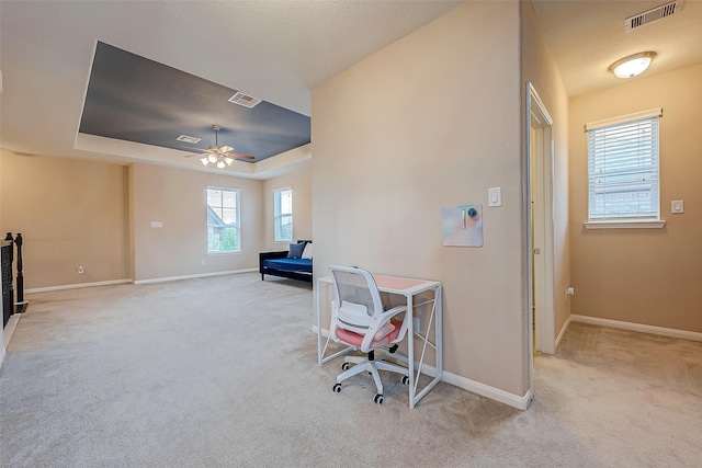 office featuring a tray ceiling, light carpet, ceiling fan, and a healthy amount of sunlight