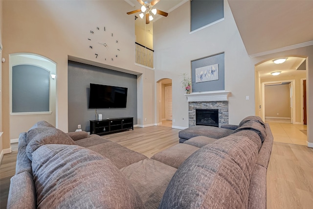 living room with crown molding, a fireplace, a towering ceiling, and light hardwood / wood-style floors