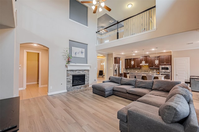 living room featuring ceiling fan, sink, a towering ceiling, light hardwood / wood-style floors, and a fireplace