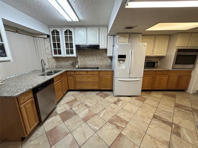 kitchen featuring backsplash, light stone counters, a textured ceiling, stainless steel appliances, and sink