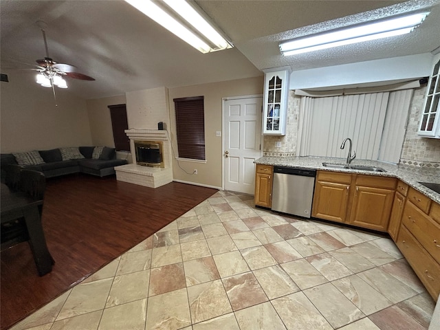 kitchen with sink, stainless steel dishwasher, ceiling fan, a fireplace, and a textured ceiling