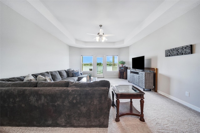 carpeted living room with ceiling fan and a tray ceiling