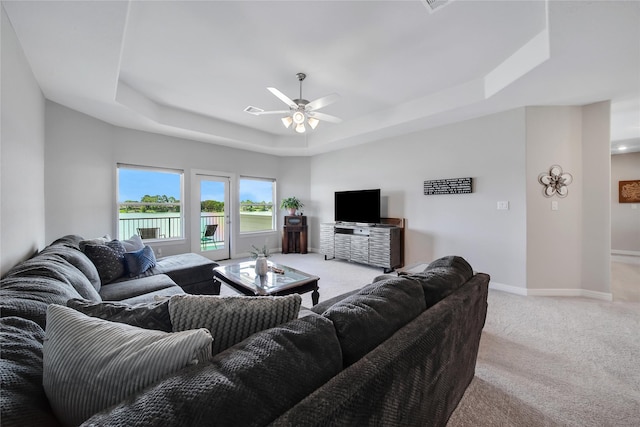 living room with a tray ceiling, ceiling fan, and light colored carpet