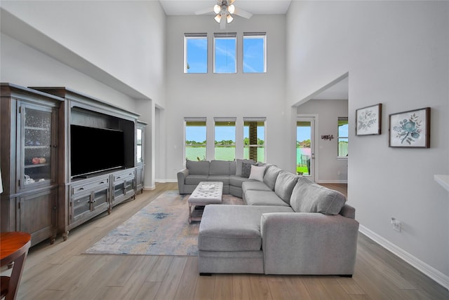 living room featuring ceiling fan, a towering ceiling, and light wood-type flooring