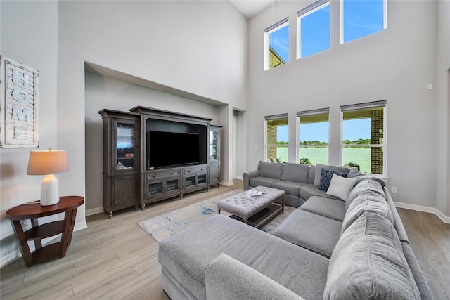 living room with plenty of natural light, a towering ceiling, and light wood-type flooring