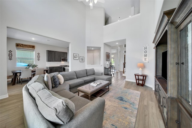 living room featuring a high ceiling, light hardwood / wood-style floors, and ceiling fan