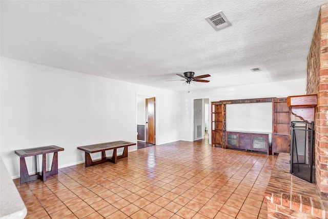 unfurnished living room featuring ceiling fan, a fireplace, light tile patterned floors, and a textured ceiling