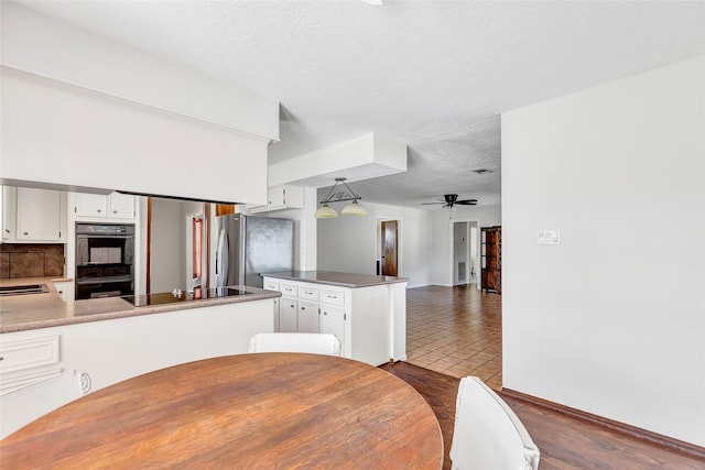 kitchen featuring kitchen peninsula, decorative light fixtures, white cabinets, and black appliances