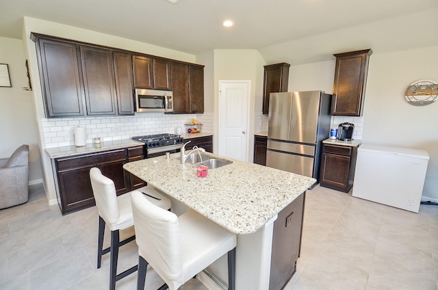 kitchen featuring sink, light stone countertops, an island with sink, appliances with stainless steel finishes, and tasteful backsplash