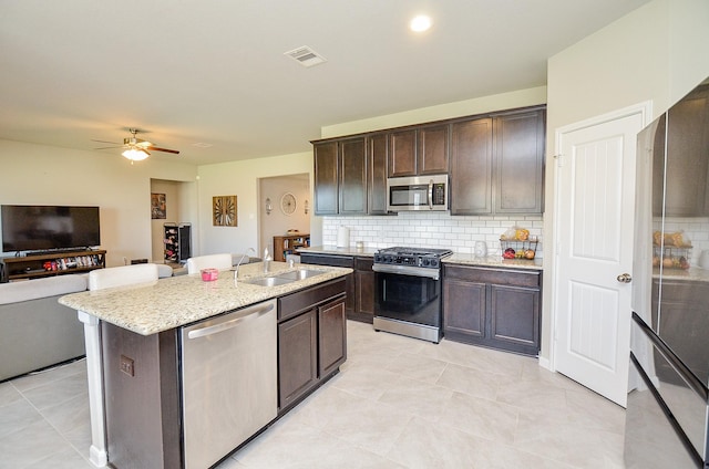 kitchen featuring appliances with stainless steel finishes, backsplash, a center island with sink, and sink