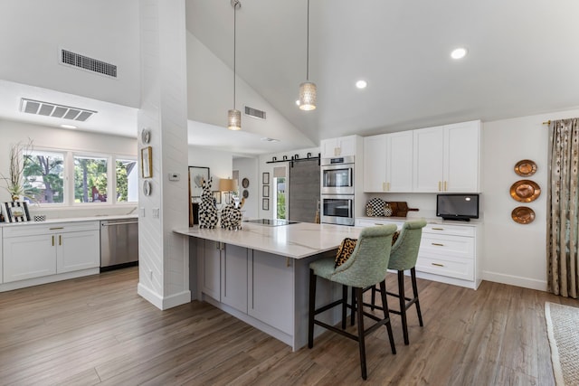 kitchen with stainless steel appliances, white cabinetry, a barn door, and a breakfast bar area