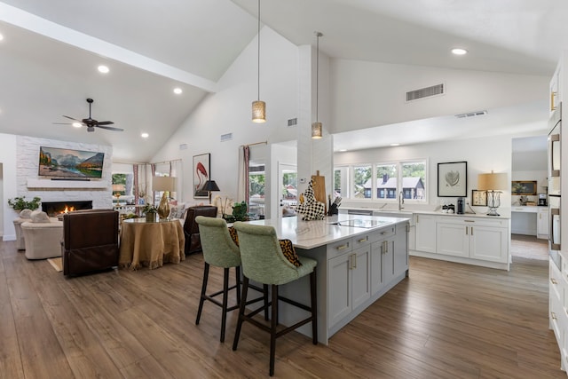 kitchen featuring decorative light fixtures, high vaulted ceiling, white cabinetry, ceiling fan, and a stone fireplace