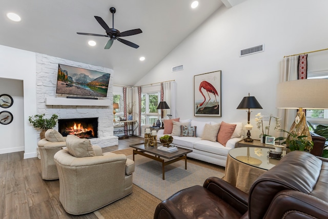 living room featuring ceiling fan, light wood-type flooring, a stone fireplace, and high vaulted ceiling