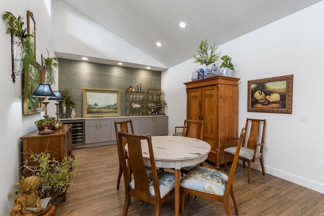 dining room featuring high vaulted ceiling, indoor bar, wine cooler, and light hardwood / wood-style flooring