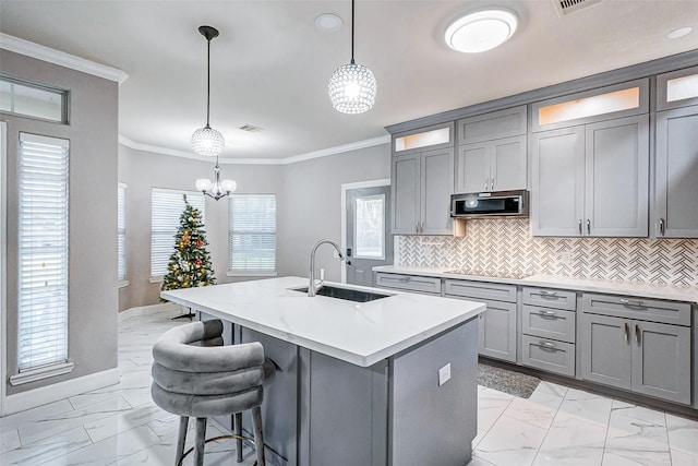 kitchen featuring tasteful backsplash, ornamental molding, sink, pendant lighting, and a center island with sink