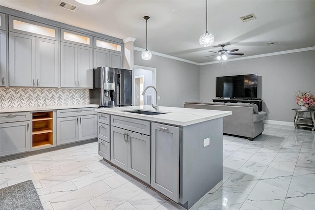 kitchen featuring gray cabinetry, a center island with sink, sink, hanging light fixtures, and stainless steel fridge with ice dispenser