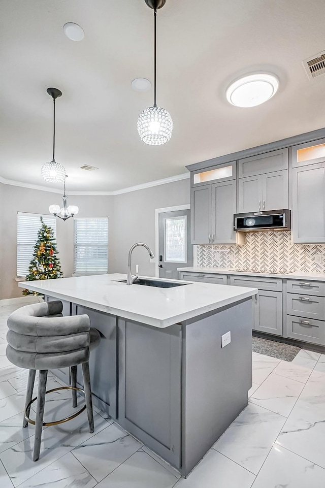 kitchen featuring sink, range hood, decorative light fixtures, a kitchen island with sink, and ornamental molding