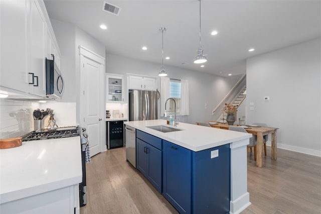 kitchen featuring sink, blue cabinets, an island with sink, white cabinets, and appliances with stainless steel finishes