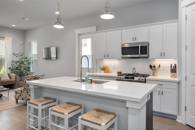 kitchen with white cabinetry, sink, an island with sink, decorative light fixtures, and appliances with stainless steel finishes