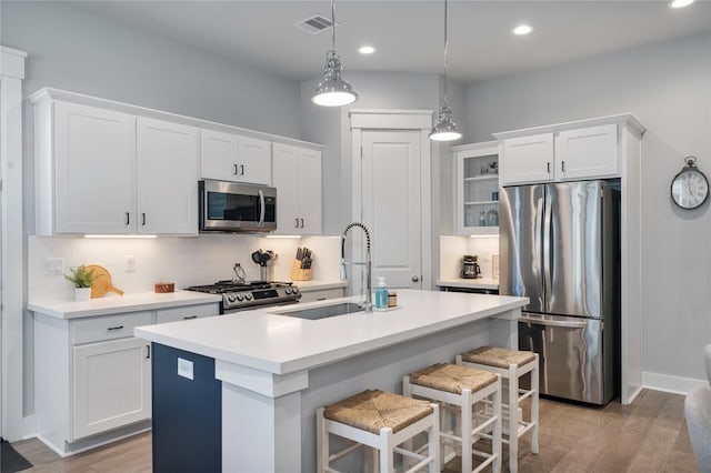 kitchen featuring pendant lighting, backsplash, white cabinets, a center island with sink, and appliances with stainless steel finishes