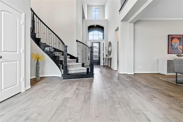 foyer entrance featuring crown molding, a healthy amount of sunlight, a high ceiling, and light hardwood / wood-style floors