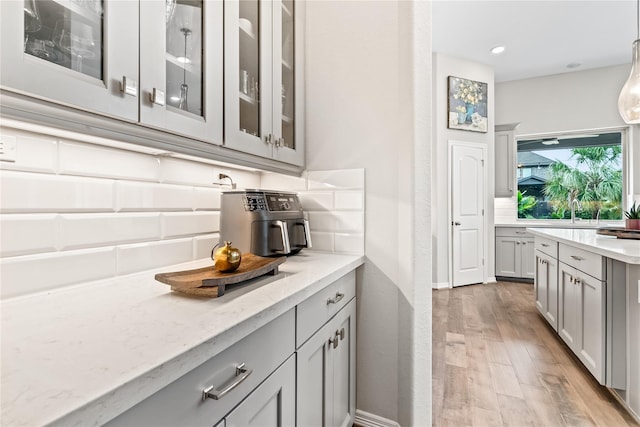 bar with pendant lighting, gray cabinets, light stone counters, and light hardwood / wood-style flooring