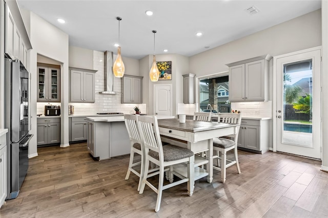 kitchen featuring a center island, wall chimney exhaust hood, gray cabinets, stainless steel fridge, and decorative light fixtures